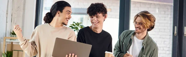 Jeunes hommes excités engagés dans une discussion animée sur un ordinateur portable dans un espace de coworking, bannière de démarrage — Photo de stock