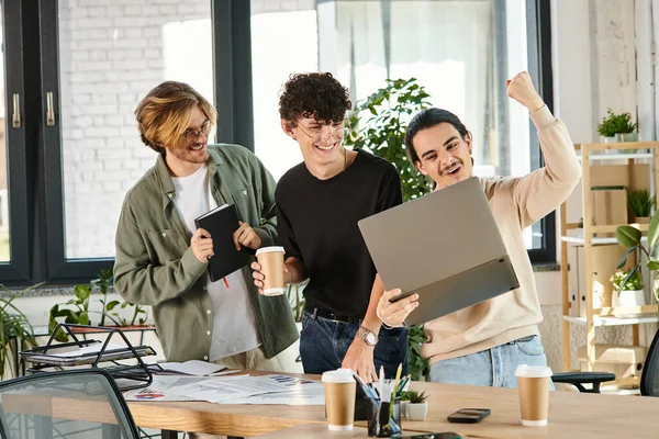 Trois jeunes hommes engagés dans une discussion animée sur un ordinateur portable dans un espace de coworking, succès — Photo de stock