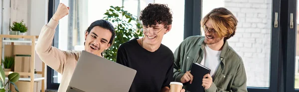 Трое молодых людей, участвующих в оживленной дискуссии за ноутбуком в коворкинге, баннер успеха — стоковое фото
