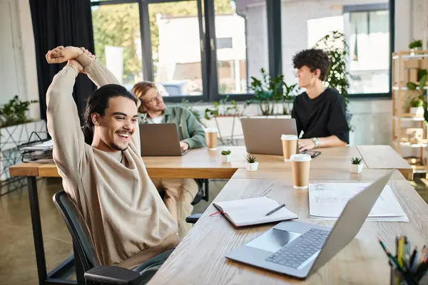 Joyeux jeune entrepreneur analyser les données sur ordinateur portable avec des collègues flous dans un espace de travail moderne — Photo de stock