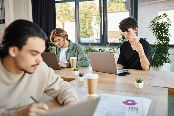Jóvenes profesionales profundamente enfocados mientras trabajan en computadoras portátiles en un espacio de coworking, borroso en primer plano - foto de stock