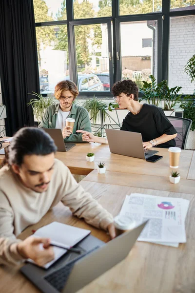 De jeunes professionnels partageant des idées près d'ordinateurs portables dans un espace de coworking, au premier plan flou — Photo de stock