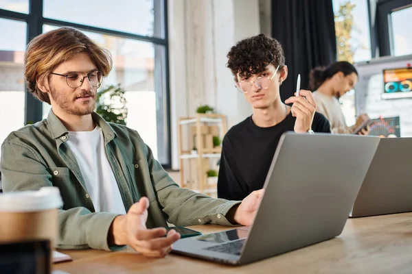 Jovem equipe de inicialização profundamente focada enquanto trabalhava em laptops no espaço de co-trabalho moderno, homens em 20s — Fotografia de Stock