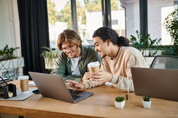 Joyful startup team members discussing project and working on laptops in coworking space, men in 20s — Stock Photo