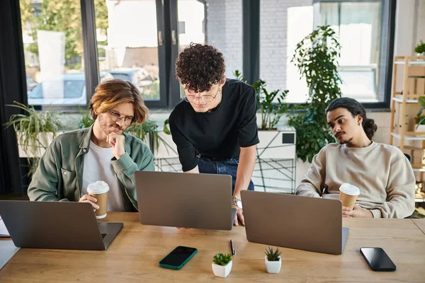 Engaged young team analyzing content together on laptops in a sunlit coworking space, men in 20s — Stock Photo