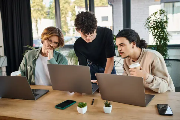 Engaged young men in 20s analyzing startup together on laptops in a sunlit coworking space — Stock Photo