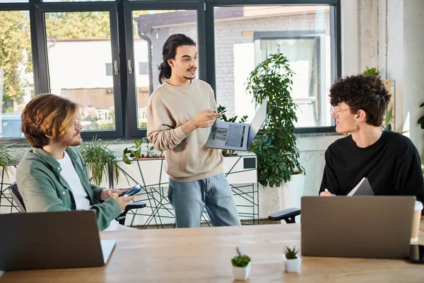 Team lead discussing project details and pointing at colleagues in a workspace, men in their 20s — Stock Photo