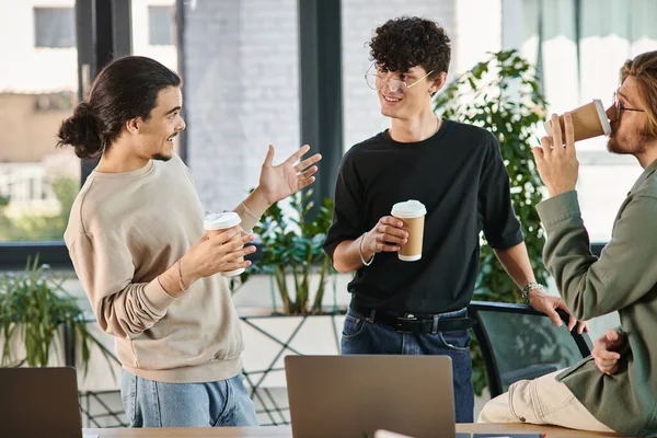 Дружеский разговор между тремя молодыми коллегами, держащими кофе, чтобы пойти в современный офис, стартап — стоковое фото