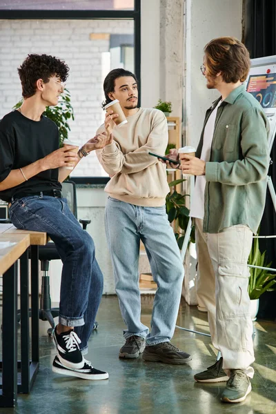 Giovani uomini sulla ventina che condividono idee e tengono il caffè per andare in ufficio moderno, startup team — Foto stock