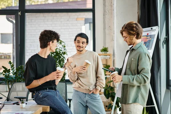 Jeunes hommes dans la vingtaine partageant des idées et bavardant autour d'un café pour aller dans un bureau moderne, équipe de démarrage — Photo de stock