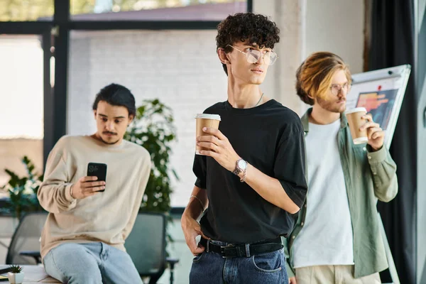 Centrarse en el hombre de pelo rizado contemplativamente bebiendo café con sus compañeros de trabajo en un entorno de oficina - foto de stock