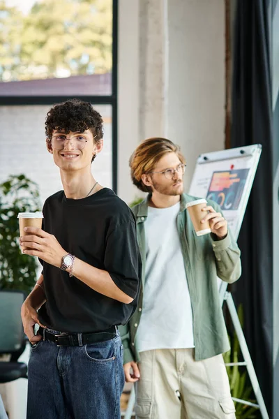 Centrarse en el hombre de pelo rizado feliz contemplativamente bebiendo café con compañeros de trabajo en un entorno de oficina - foto de stock