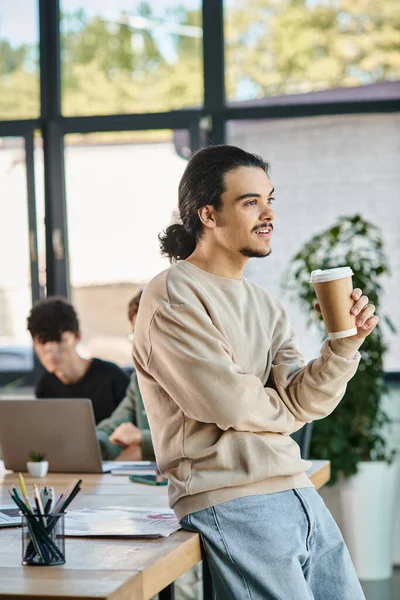 Junger Mann in seinen Zwanzigern genießt seine Kaffeepause in einem geschäftigen Startup-Büro, professionell bei der Arbeit — Stockfoto