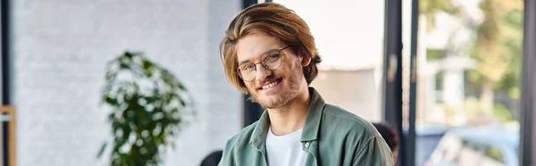 Cheerful young businessman in glasses standing in modern coworking space, horizontal banner — Stock Photo