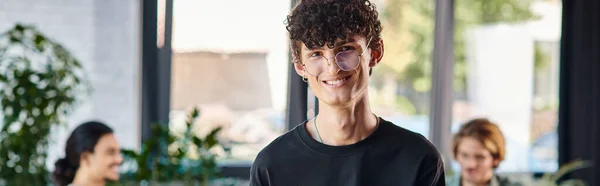 Glücklicher und lockiger Mann, der in einem dynamischen Büroraum lächelt und Notizen macht, Startup-Banner — Stockfoto