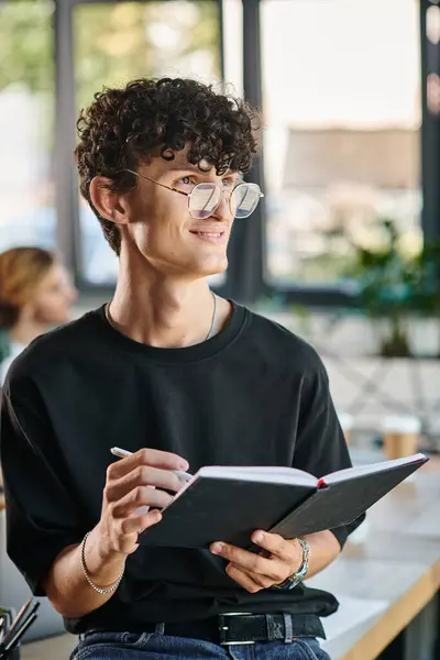 Curly-haired startup team member with glasses smiling and taking notes in a dynamic office space — Stock Photo