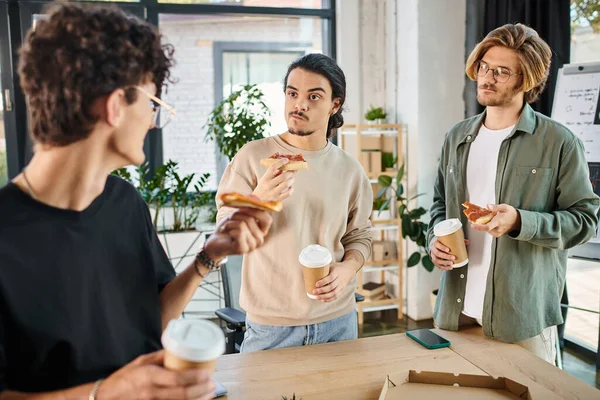 Hommes douteux manger de la pizza dans une atmosphère de bureau détendue, jeune équipe de démarrage ayant pause déjeuner — Photo de stock