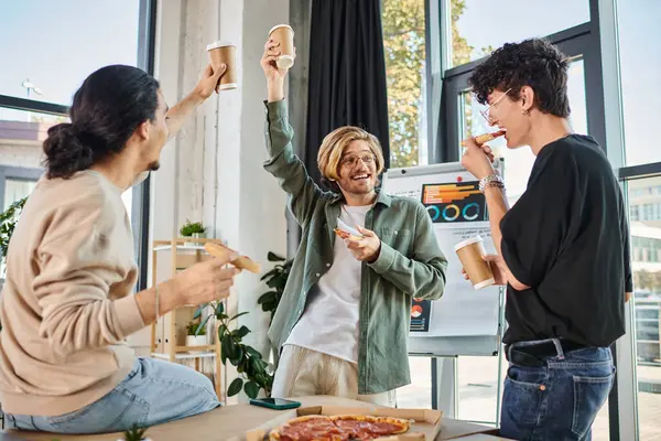 Junge Männer stoßen mit Kaffee und Pizza in freundlicher und entspannter Atmosphäre an, Team in der Mittagspause — Stockfoto