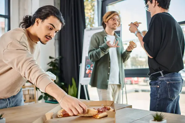 Young man with coffee to go taking slice of pizza in relaxed office atmosphere, lunch break — Stock Photo