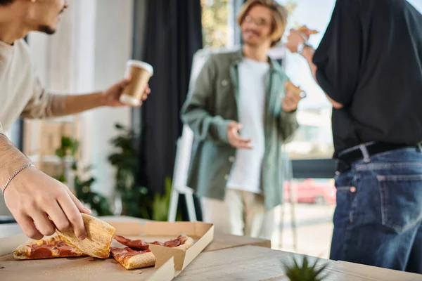 Focus on team member with coffee taking slice of pizza in friendly office atmosphere, lunch break — Stock Photo