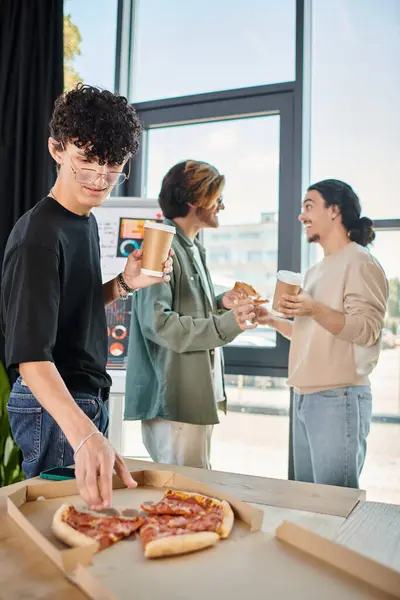 Curly team member with coffee taking slice of pizza in friendly office atmosphere, lunch break — Stock Photo
