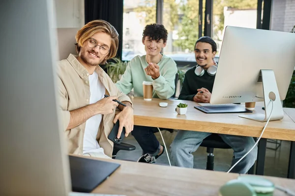 Счастливая творческая команда сосредоточена на пост-производственной работе, глядя на монитор в офисе, мужчины в 20 лет — стоковое фото