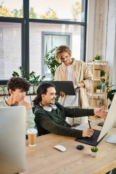 Felice team di post produzione focalizzato su un progetto di ritocco in ufficio, uomo con laptop vicino ai colleghi — Foto stock