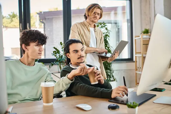 Post production team of young men focused on a retouching project on monitor in a well-lit office — Stock Photo