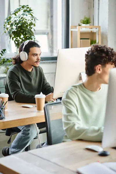 Junge männliche Berufstätige mit Kopfhörern bei der Retusche am Computer in der Nähe von Kollegen beschäftigt — Stockfoto