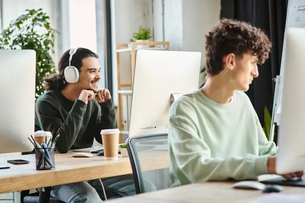Joven con auriculares dedicados al trabajo de retoque en una computadora cerca de un colega en la oficina - foto de stock