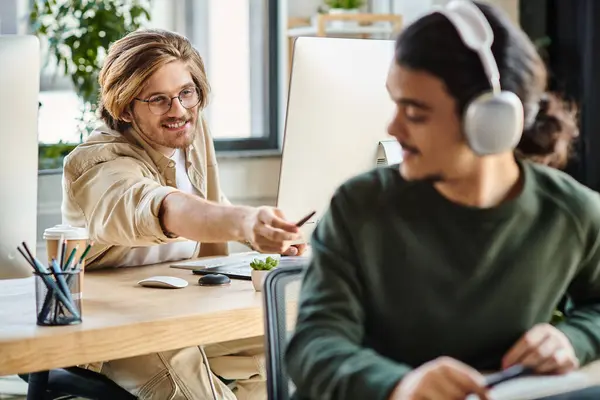 Cheerful male professional in glasses passing his stylus pen to blurred coworker in headphones — Stock Photo