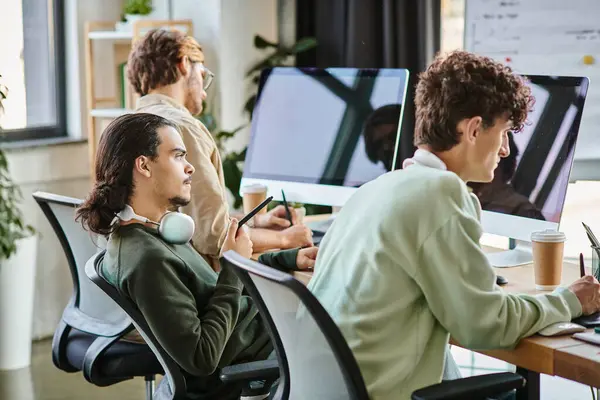 Junger Mann mit Kopfhörern bearbeitet Fotos auf Tablet und blickt im Startup-Büro auf Monitor — Stockfoto