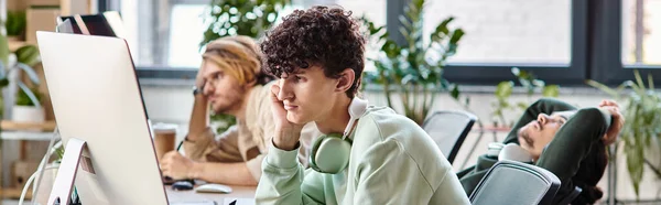 Young curly-haired man editing photos on tablet and looking at monitor in startup office, banner — Stock Photo