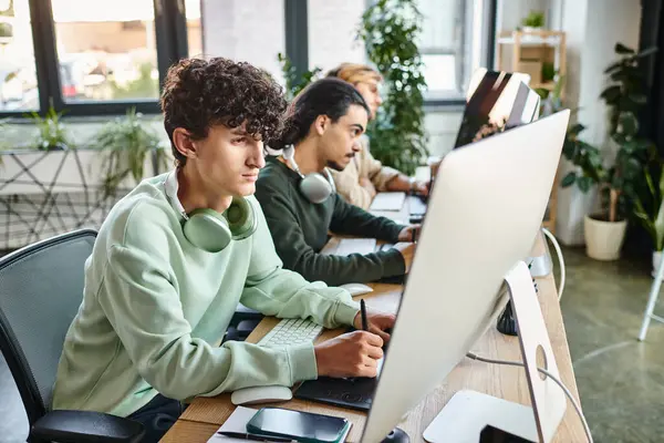 Focused curly-haired man editing photos on tablet and looking at monitor in modern startup office — Stock Photo
