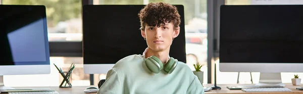 Encaracolado jovem com fones de ouvido sentado perto de monitores de computador, banner pós-produção — Fotografia de Stock