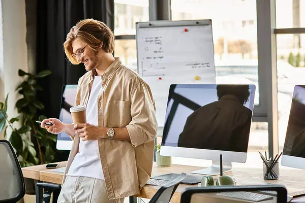 Happy man in glasses holding coffee and looking at stylus pen in office setup, post production — Stock Photo