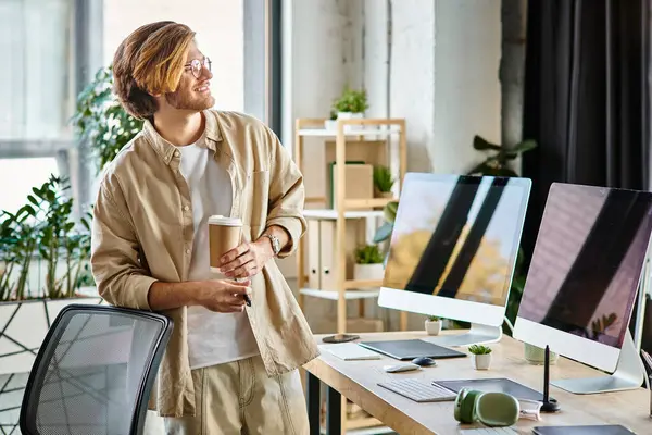 Homem alegre em óculos segurando café e caneta stylus na configuração moderna do escritório, pós-produção — Fotografia de Stock