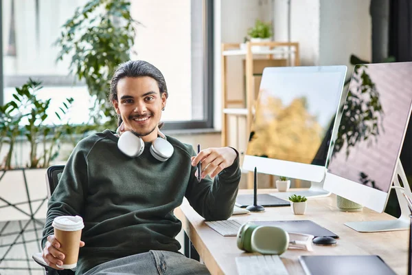 Розслаблений молодий чоловік зі стилусом ручкою і кавою посміхається на стартапі після виробництва робочого простору — стокове фото