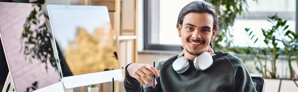 Розслаблений молодий чоловік зі стилусовою ручкою посміхається на стартапі постпродакшн робочого простору, банер — стокове фото