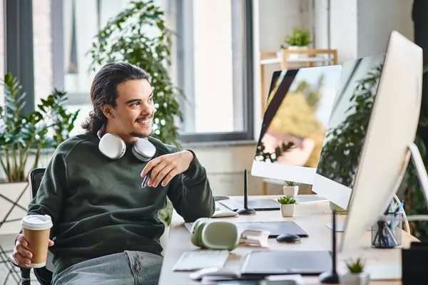Молодой человек со стилус ручкой и кофе улыбается и смотрит на монитор в пост-производственном рабочем пространстве — стоковое фото