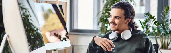 Чоловік зі стилусом ручкою і кавою посміхається і дивиться на монітор в пост-продакшн офісі, банер — стокове фото