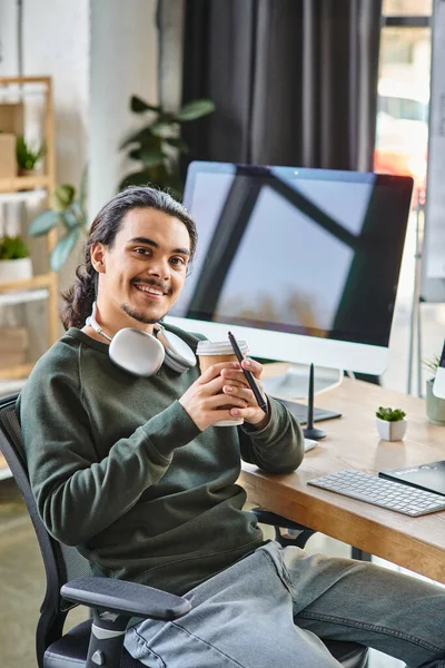 Розслаблений молодий чоловік зі стилусом ручкою і кавою посміхається на стартапі після виробництва робочого простору — стокове фото
