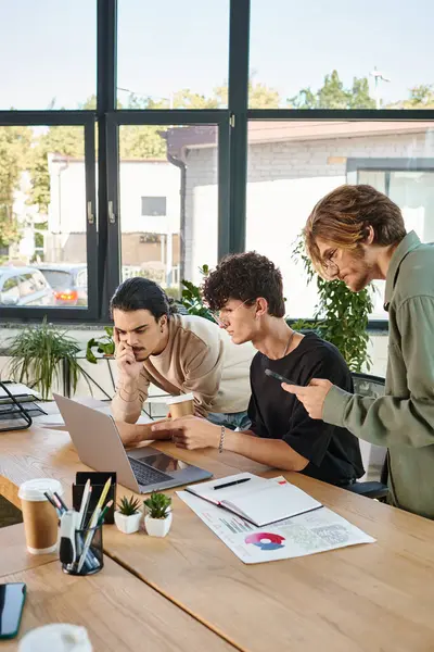 Three team members engaged in project discussion in startup workspace, men in 20s looking at laptop — Stock Photo