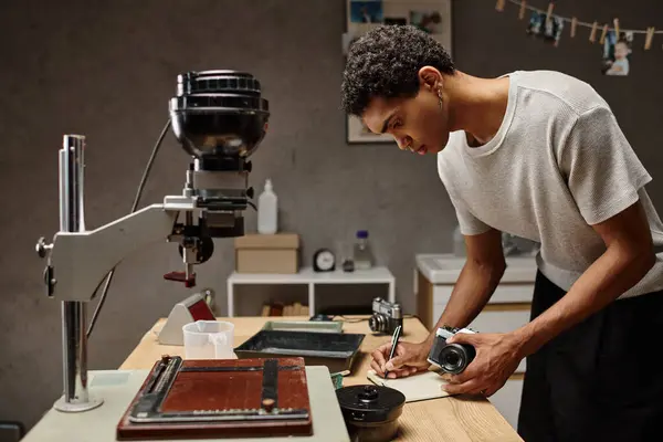 Fotógrafo afro-americano imerso em escrita enquanto segurava câmera analógica no estúdio de fotografia — Fotografia de Stock