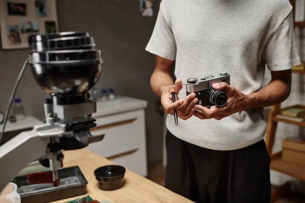 Recortado de hombre negro Sujetando intencionadamente una cámara analógica y un bolígrafo mientras está de pie en un laboratorio fotográfico - foto de stock
