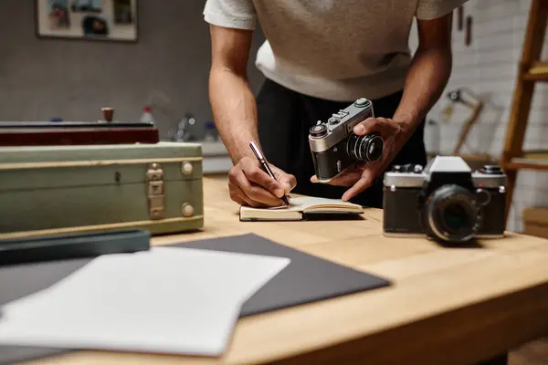 Fotógrafo afroamericano recortado inmerso en la escritura sosteniendo su cámara analógica en el estudio de fotografía - foto de stock