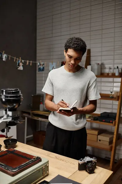 Young african american guy immersed in writing standing near analog camera in photo studio — Stock Photo