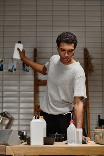 Young african american guy choosing chemical solution in darkroom, film development process — Stock Photo