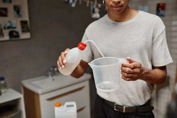 Обрезанный африканский американец разливает химический раствор в измерительную чашку, аналоговую пленку — стоковое фото