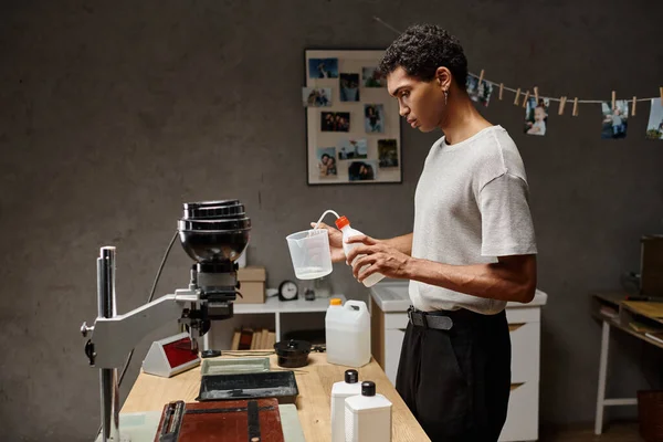 Jeune homme afro-américain versant une solution chimique dans une tasse à mesurer, développement de film analogique — Photo de stock